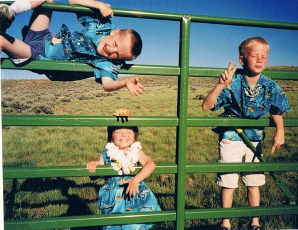 Three young kids in matching blue Hawaiian shirts climbing a green metal gate