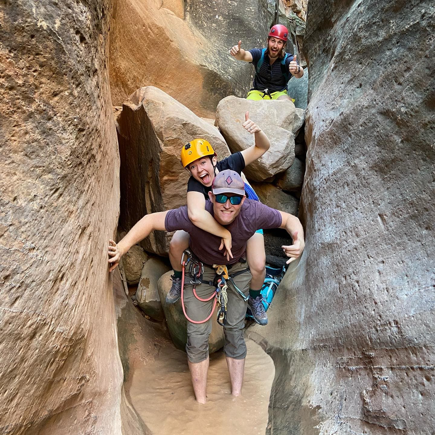 Canyoneers in helmets giving a thumbs-up while wading through a narrow slot canyon