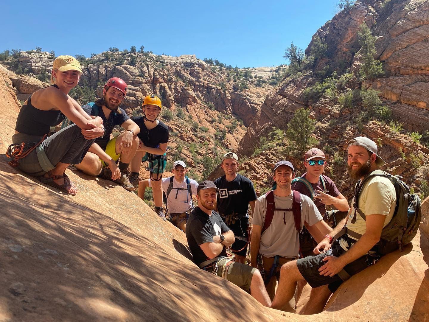 Group of nine people resting on red sandstone in a desert canyon landscape